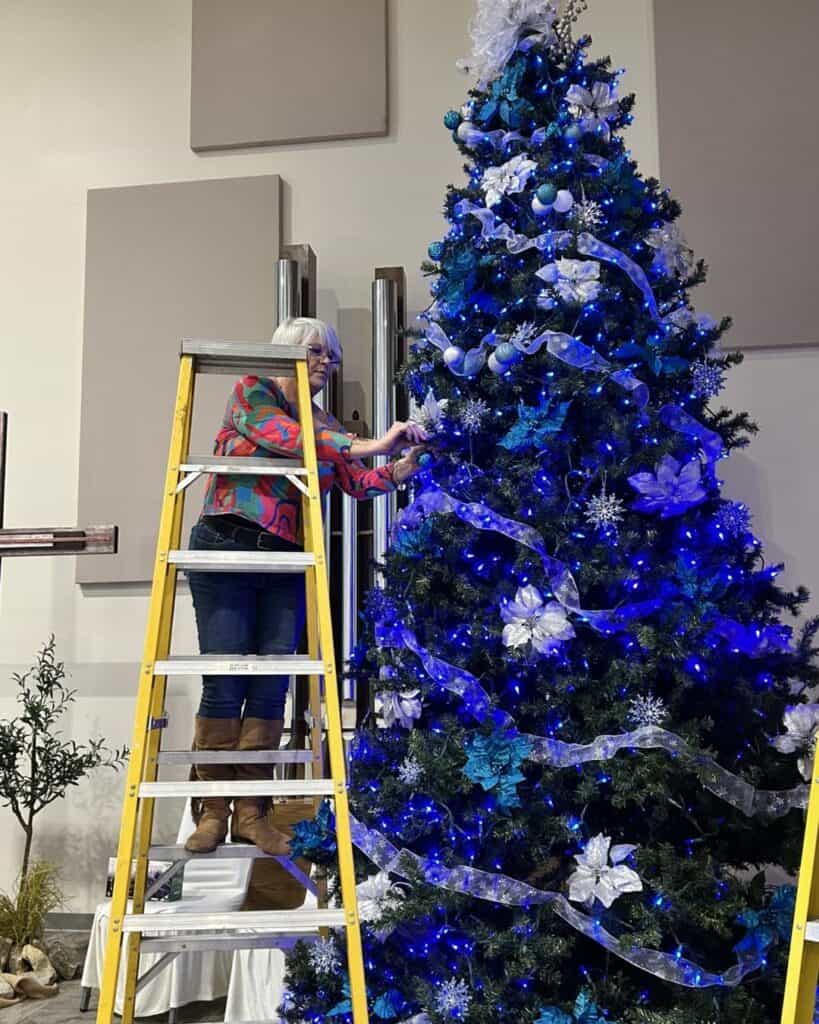 Woman decorates a large blue Christmas tree.
